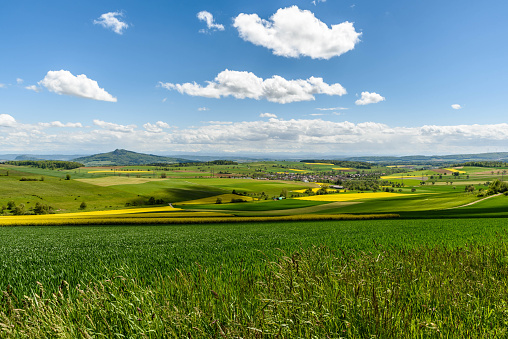 Volcanic landscape in Hegau with view of the Hohenhewen, Hohentwiel and Hohenstoffeln, three extinct volcanos in the Konstanz district in South Germany. Fields with blue cloudy sky.