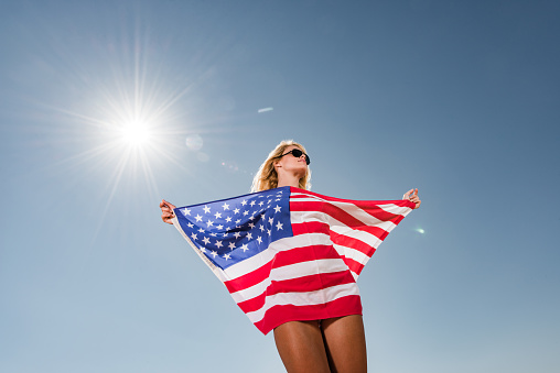 Low angle view of young woman holding American flag during sunny day. Copy space.
