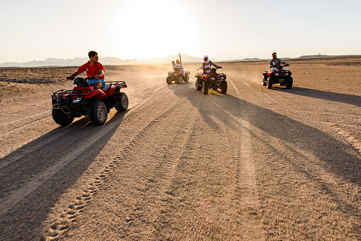 Group of happy friends driving quads in the desert at sunset. Copy space.