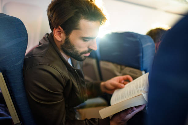 istock Young man reading a book in an airplane. 1400217171