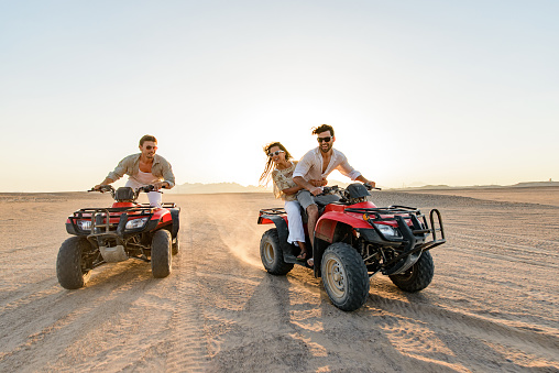 Group of happy friends having fun while driving quads in summer at the desert. Copy space.