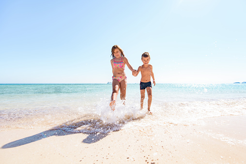Joyful children having fun while holding hands and running through sea.