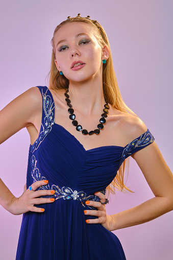 young pretty woman in blue dress and crown on pink background