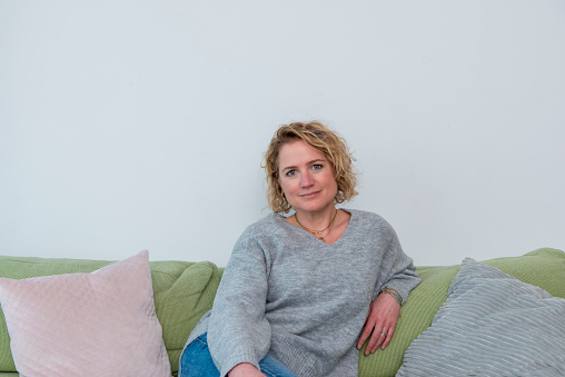 Portrait of woman sitting on couch and looking at camera. Cheerful.