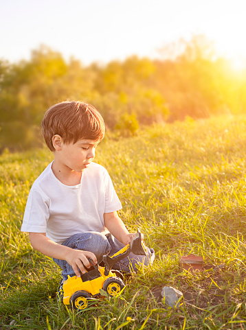 boy playing with a toy tractor outdoors in the summer in the sun