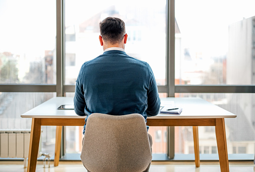 Rear view of businessman working at desk while sitting in front of windows at corporate office