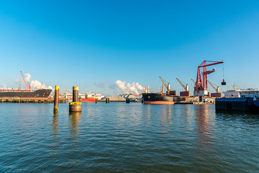 Early morning port activities with cranes and heavy industry in the back.