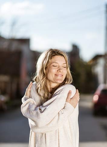 Smiling loving young woman hugging oneself. Portrait of her outdoors. Copy space.