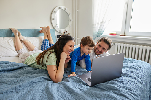 Young family having fun using laptop together in the bedroom