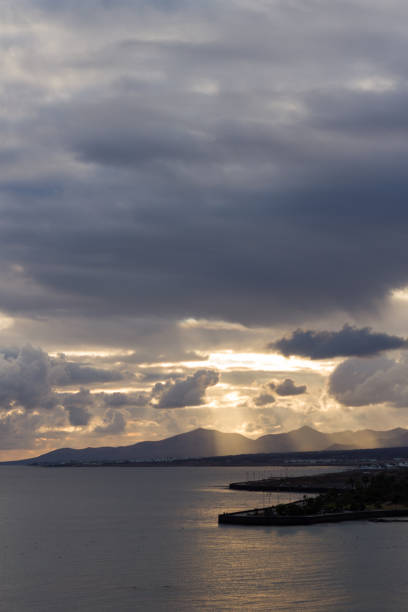 sunset in yellow sand beach with big blue clouds and ocean bathing the rocks of the coast and mountains in the background. Lanzarote, Canary Islands, Spain