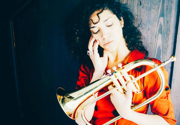The female musician with the flugelhorn. Mood photo of a female musician with the flugelhorn. She is wearing a red dress. She looks pensively at her instrument. klezmer stock pictures, royalty-free photos & images