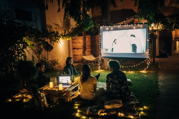 des amis regardent un film sur le vidéoprojecteur dans le jardin de la cour arrière - movie theater photos et images de collection