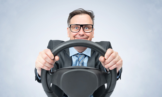 Portrait of a happy smiling man in a dark jacket, glasses and tie turning the steering wheel on a smoky light background