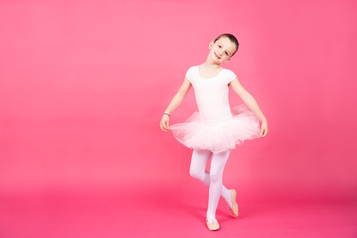 Little ballet dancer girl wearing tutu isolated on vivid pink background.
