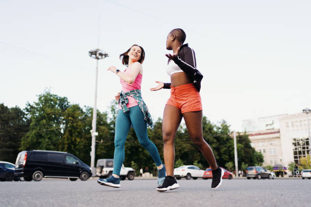 Two multiethnic girls running through the city streets, outdoor communicating. stock photo
