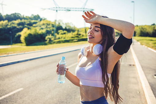 Shot of a fit young woman drinking water during a workout outdoors. Photo of a young woman taking a break to drink some water during a jog.