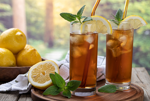 Two glasses of ice tea with slice of lemon and mint on a wooden tray with rural background