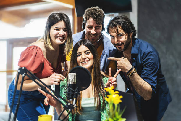 A team of four presenters greets the audience of their live streaming vlog podcast via the internet - a group of influencers speak into the microphone during a live broadcast stock photo