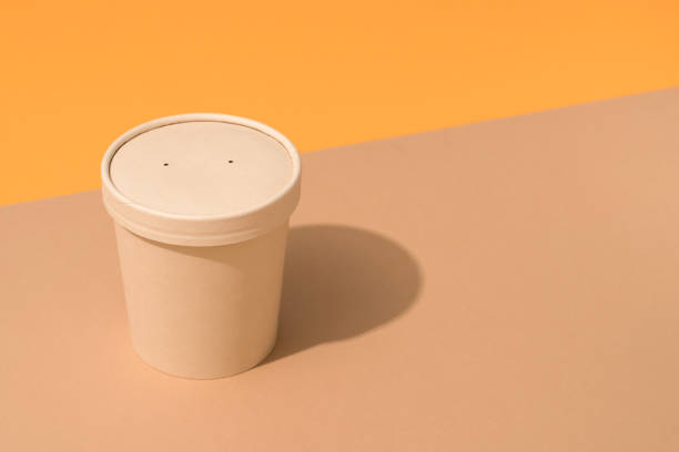 istock Brown disposable kraft paper container with paper caps for soup or beverages over light brown and orange background, mockup image. Sustainable street food packaging concept 1400246928