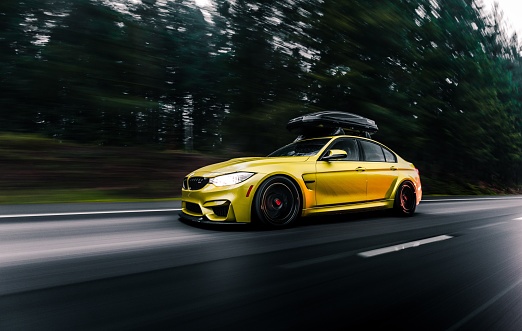 Seattle, WA, USA\n5/20/2022\nYellow BMW M4 with a roof rack driving on the highway