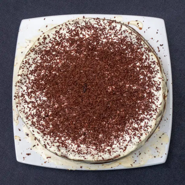 Handmade cake decorated with chocolate chips on white plate. Flat lay view