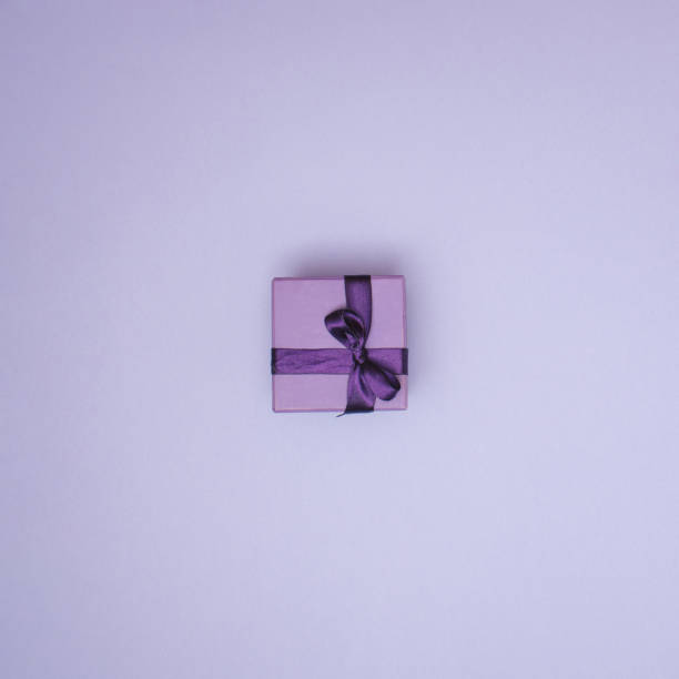 Purple gift box with ribbon on pastel purple background with copy space. Creative realistic minimal gift for Birthday or Holiday season. Present for special person or occasion.