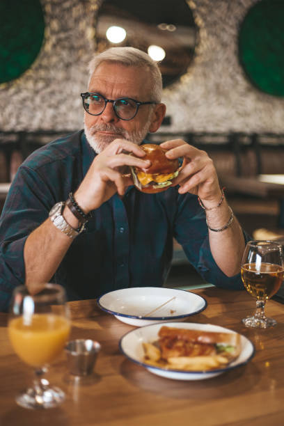istock Senior man in restaurant eating burger, lunch break. 1400251421