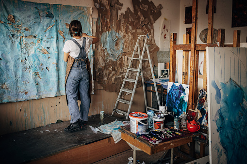 One woman, young female painter working alone in her messy art studio.
