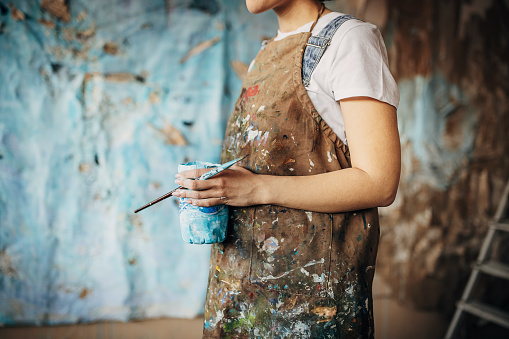 One woman, portrait of a young female painter working alone in her messy art studio.