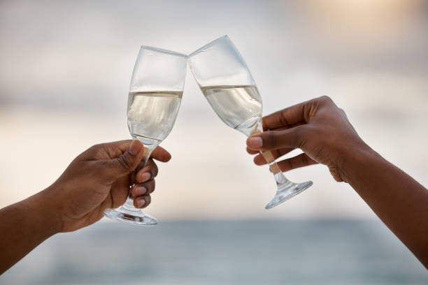 couple afro-américain buvant du champagne à la mer ensemble. petit ami attentionné et petite amie passant une journée sur la plage. mari et femme trinquant sur la plage - champagne flute champagne black wineglass photos et images de collection