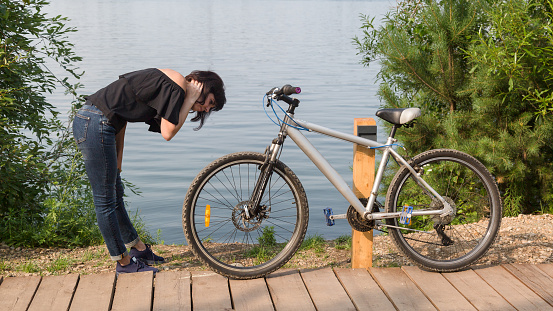 A woman by the river bent down to her bike to look at the breakdown wheel.