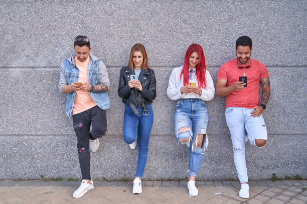 istock Group of multi-ethnic friends using their mobile phones while leaning against a wall in the street. 1400258770