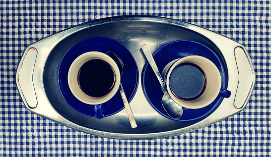 Two blue coffee cup on steel tray overhead on vintage retrò blue and white checkered tablecloth