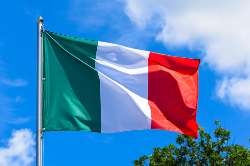 The flag of Italy is a rectangular banner with three uniform vertical stripes of green, white and red against the blue sky in summer.