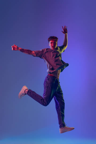 istock Young red-headed man, student jumping isolated over blue studio background in neon light. Concept of youth, fashion, emotions, facial expression 1400262360