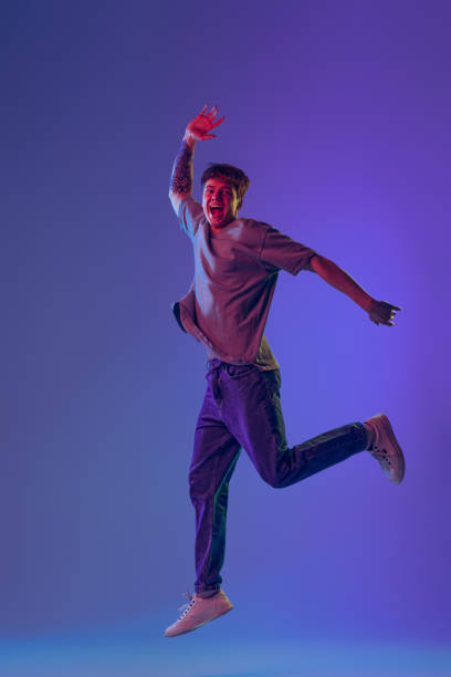 istock Young red-headed man, student jumping isolated over blue studio background in neon light. Concept of youth, fashion, emotions, facial expression 1400262366