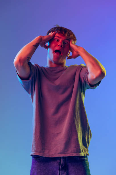 istock Young red-headed man, student grimacing isolated over blue studio background in neon light. Concept of youth, fashion, emotions, facial expression 1400262367