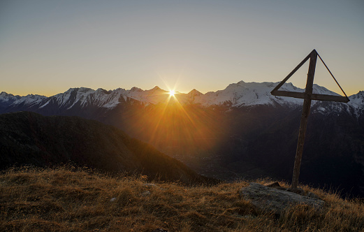 View past religious cross to sun rising over distant mountain range