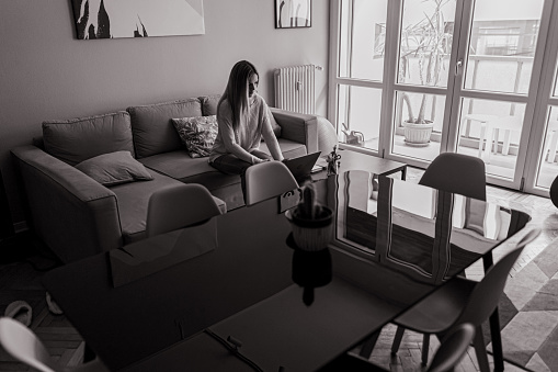 Black and white shot of home interior and woman working at home, using laptop.