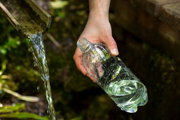 le mani maschili si avvicinano, versando acqua potabile pulita da una sorgente sacra in una bottiglia di plastica. - stream river water spring foto e immagini stock