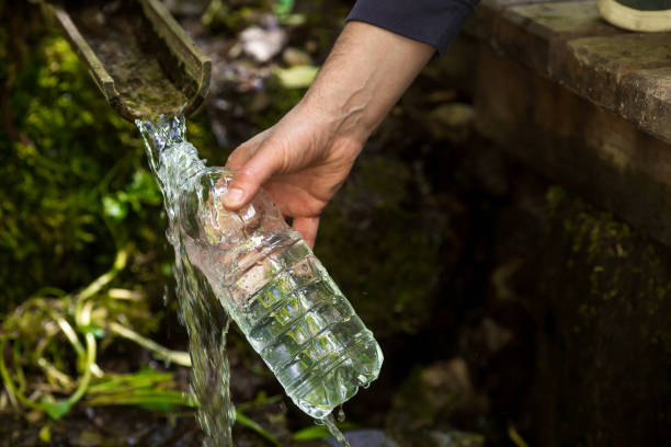 manos masculinas de cerca, vertiendo agua potable limpia de un manantial sagrado en una botella de plástico. - waterfall river stream mountain fotografías e imágenes de stock