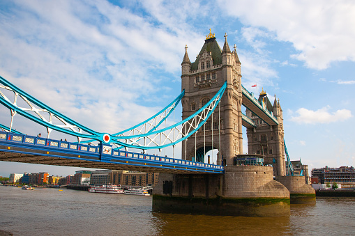 The famous Tower Bridge, on the Thames river, in London, England, on a day with blue sky and white puffy clouds.