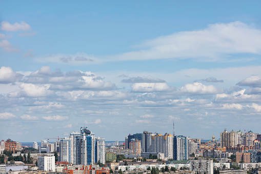 Small soft clouds float in the blue sky over a modern city with new high-rise residential neighborhoods on a sunny summer day. Copy space.
