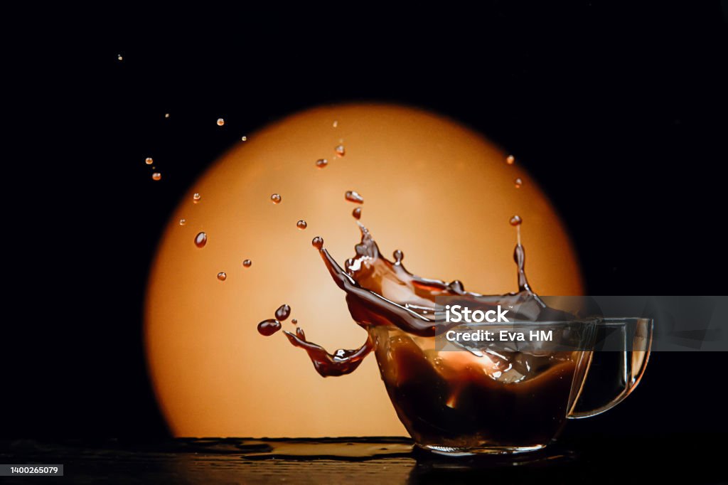 coffee splashed in cup as lump of sugar falls on dark, warm background Black Color Stock Photo