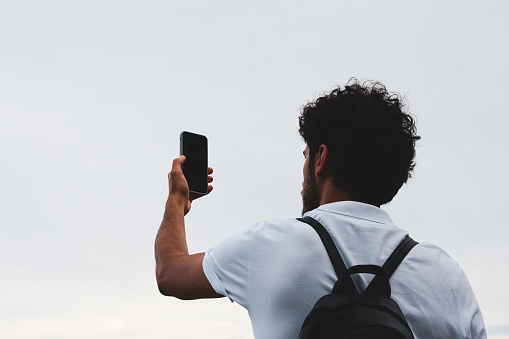 Tourist with white polo shirt and backpack holding a smartphone. Video calls and modern travel.
