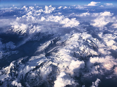 Chamonix, France - May 18, 2022. View of the Alps mountain range from the sky. Between the clouds clinging to the Mont-Blanc massif, snow-capped mountains, glaciers and rocky peaks are visible.
