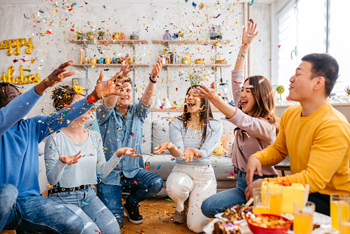 Group of young people celebrating their friend's birthday indoors. Throwing confetti