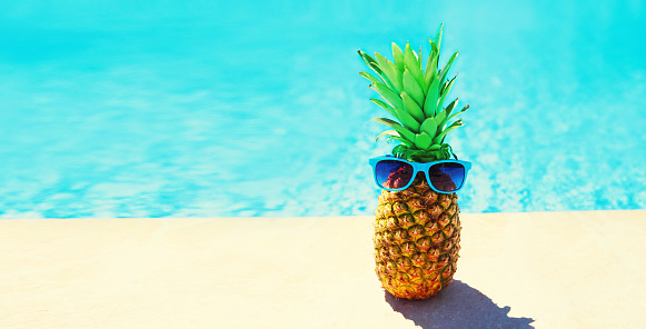 Funny pineapple with sunglasses on blue water pool background, summer holidays, vacation and food concept