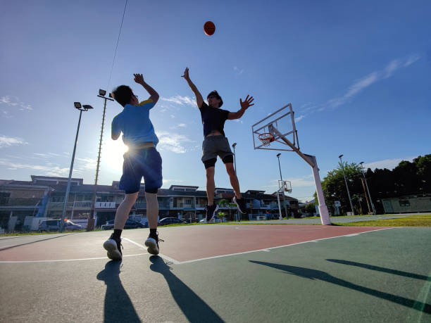 backlit Asian chinese father jumping blocking son shooting playing basketball outdoors during weekend morning
