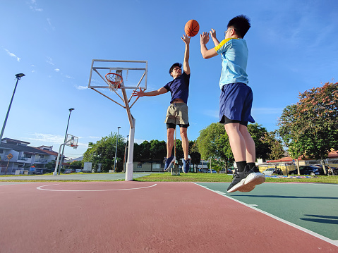 backlit Asian chinese father jumping blocking son shooting playing basketball outdoors during weekend morning